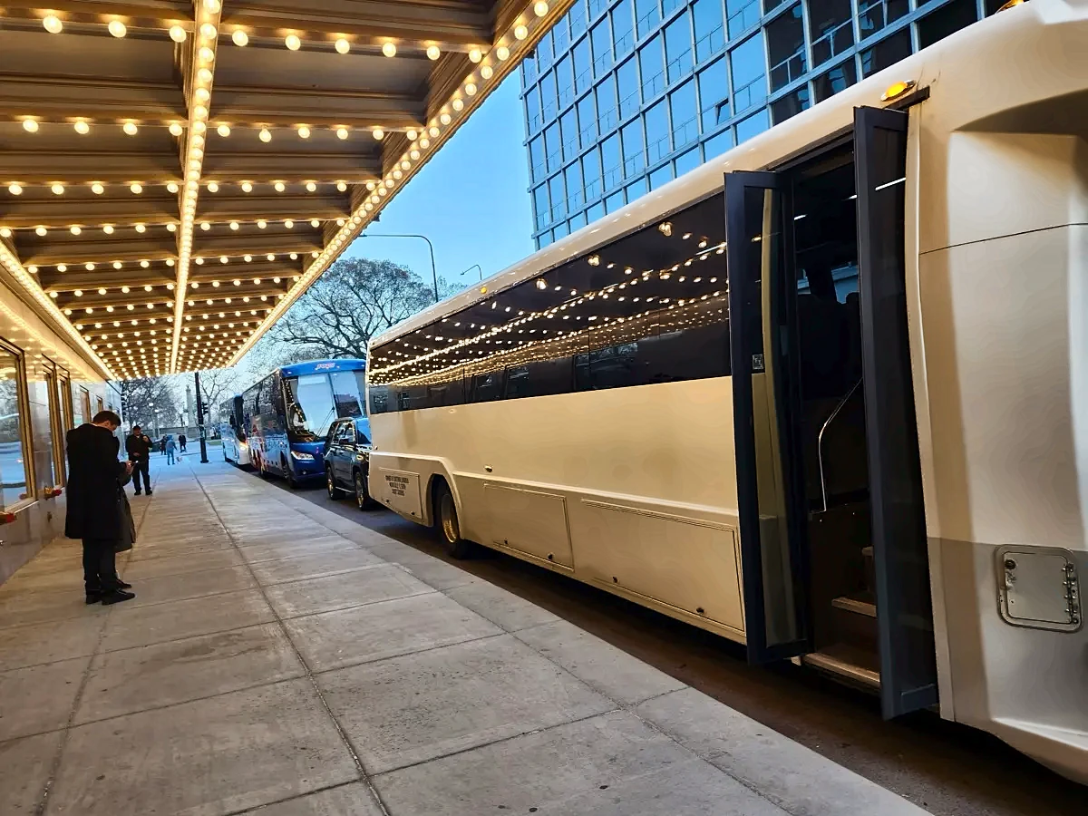 White motor coach at the curb under a lit theater marquee