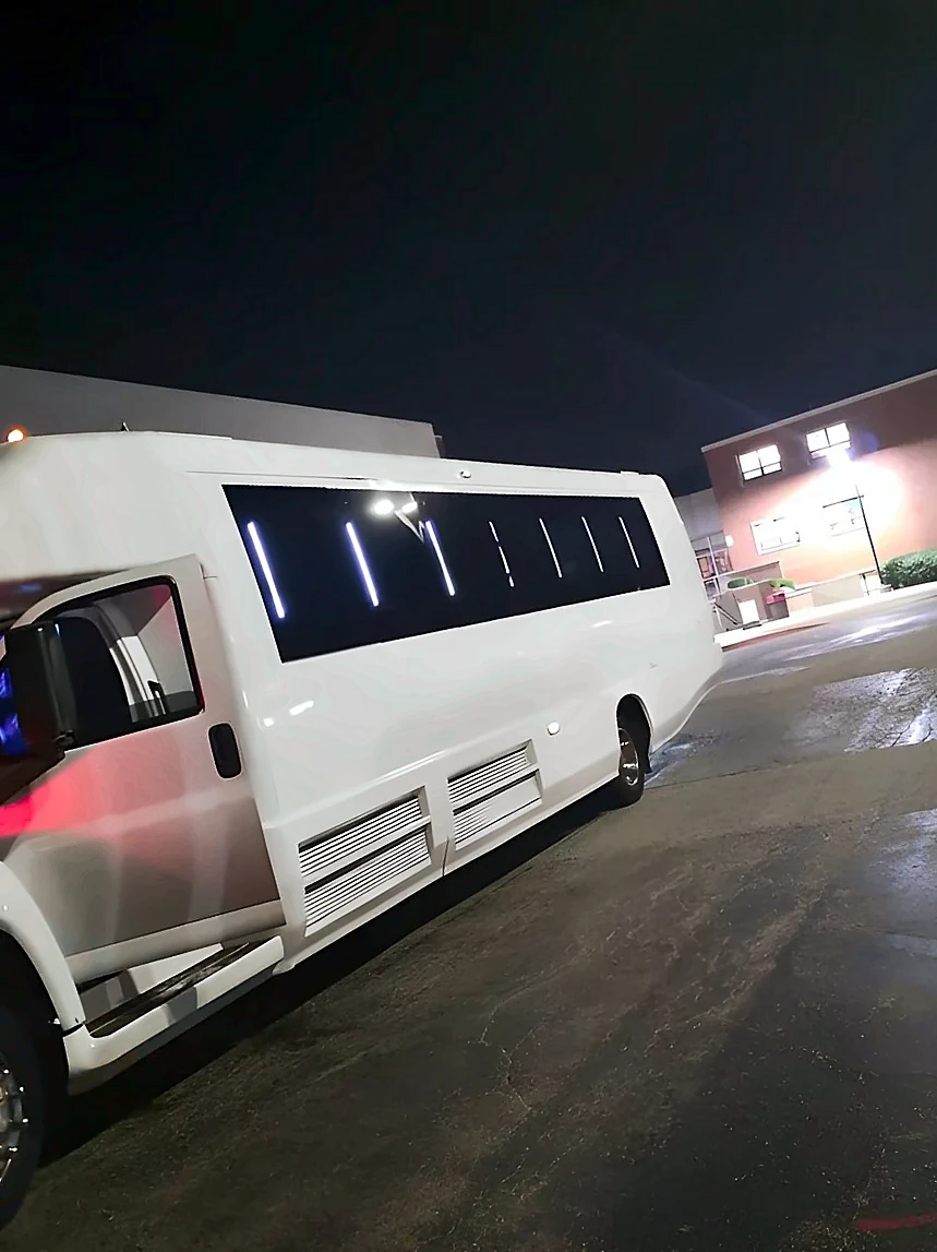 White 34-passenger party bus parked at night with interior lights on