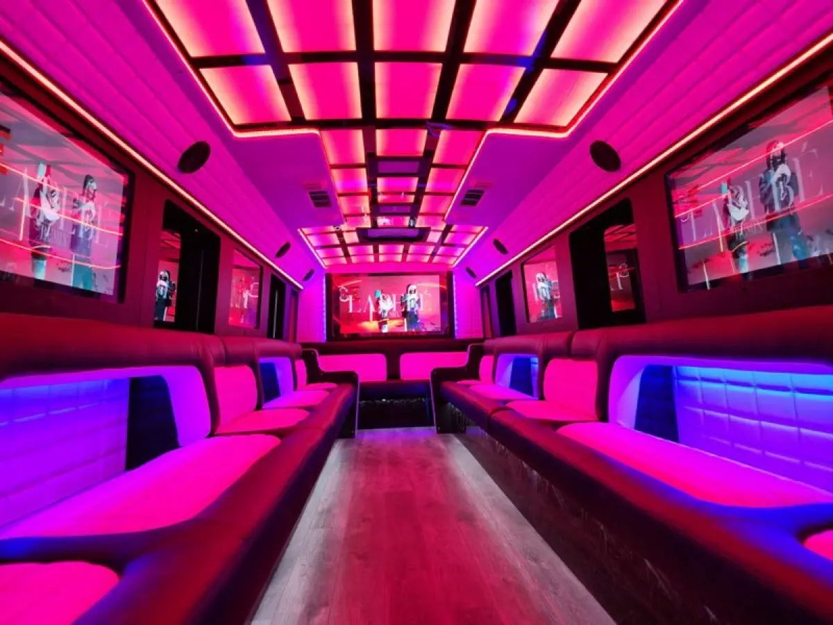 Party bus interior with a pink and red LED ceiling and wraparound seats